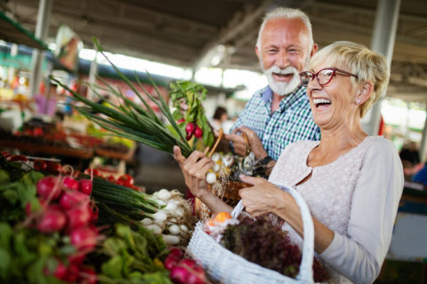 Smiling female and male couple holding basket with vegetables at the grocery shop.