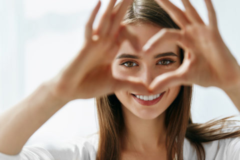 Healthy Eyes And Vision. Portrait Of Beautiful Happy Woman Holding Heart Shaped Hands Near Eyes. Closeup Of Smiling Girl With Healthy Skin Showing Love Sign.. 