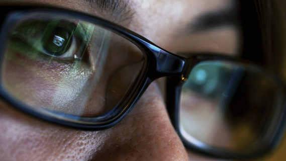 Woman wearing glasses looking at a computer monitor with a screen reflection in her eye glasses.